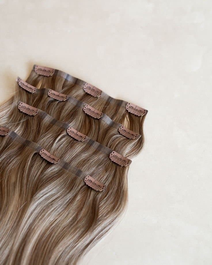 Four seamless clip-in hair extension wefts laid flat, each with brown snap clips, in a warm brown balayage shade