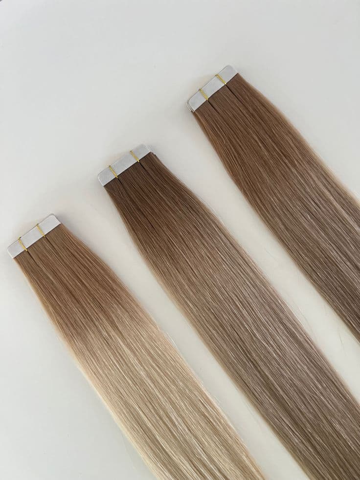 Trois extensions tape-in dans des nuances brunes balayées, posées à plat sur un fond blanc