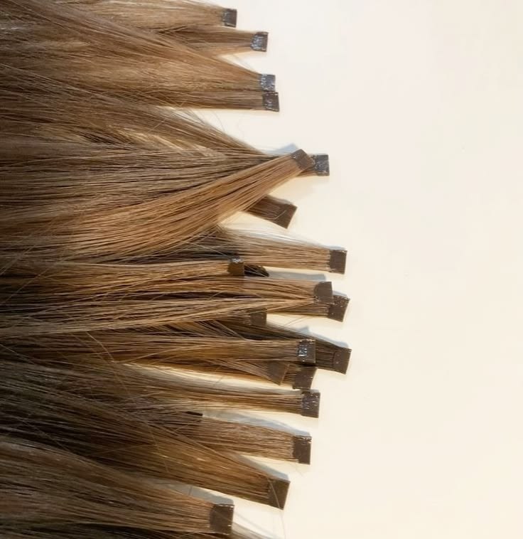 Des mèches à embout en kératine dans plusieurs teintes Mèches de cheveux châtains avec embouts en kératine, posées côte à côte sur un fond crème
